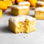 A slice of lemon cake with a bite missing and lemons in the background