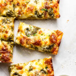 Slices of Cheesy Pesto Garlic Bread next to a small bowl of freshly grated parmesan