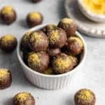 No-Bake Cheesecake Balls coated in chocolate and sprinkled with graham cracker crumbs sitting in a small bowl.