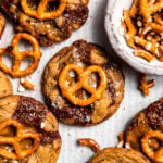 Close up of freshly baked Salted Caramel Pretzel Chocolate Chip Cookies on a baking sheet next to chopped pretzels.