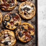 Freshly baked Oreo chocolate chip cookies on a cookie sheet surrounded by Oreo crumbs.