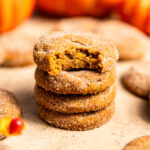 A stack of pumpkin snickerdoodles with a bite missing from the top cookie.