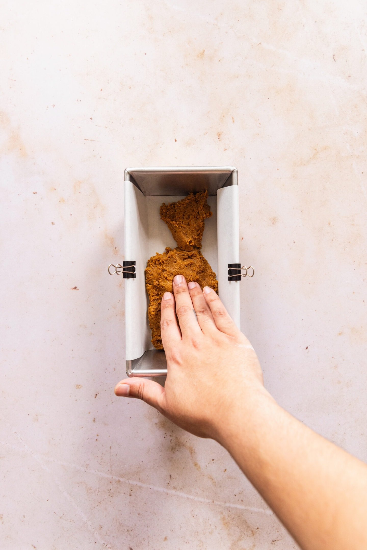 Cookie dough being pressed by hand into prepared loaf pan.