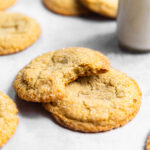 Sugar cookies stacked on top of each other with a bite missing from one next to a glass of milk.
