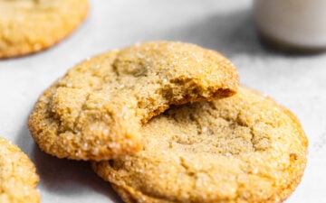 Sugar cookies stacked on top of each other with a bite missing from one next to a glass of milk.
