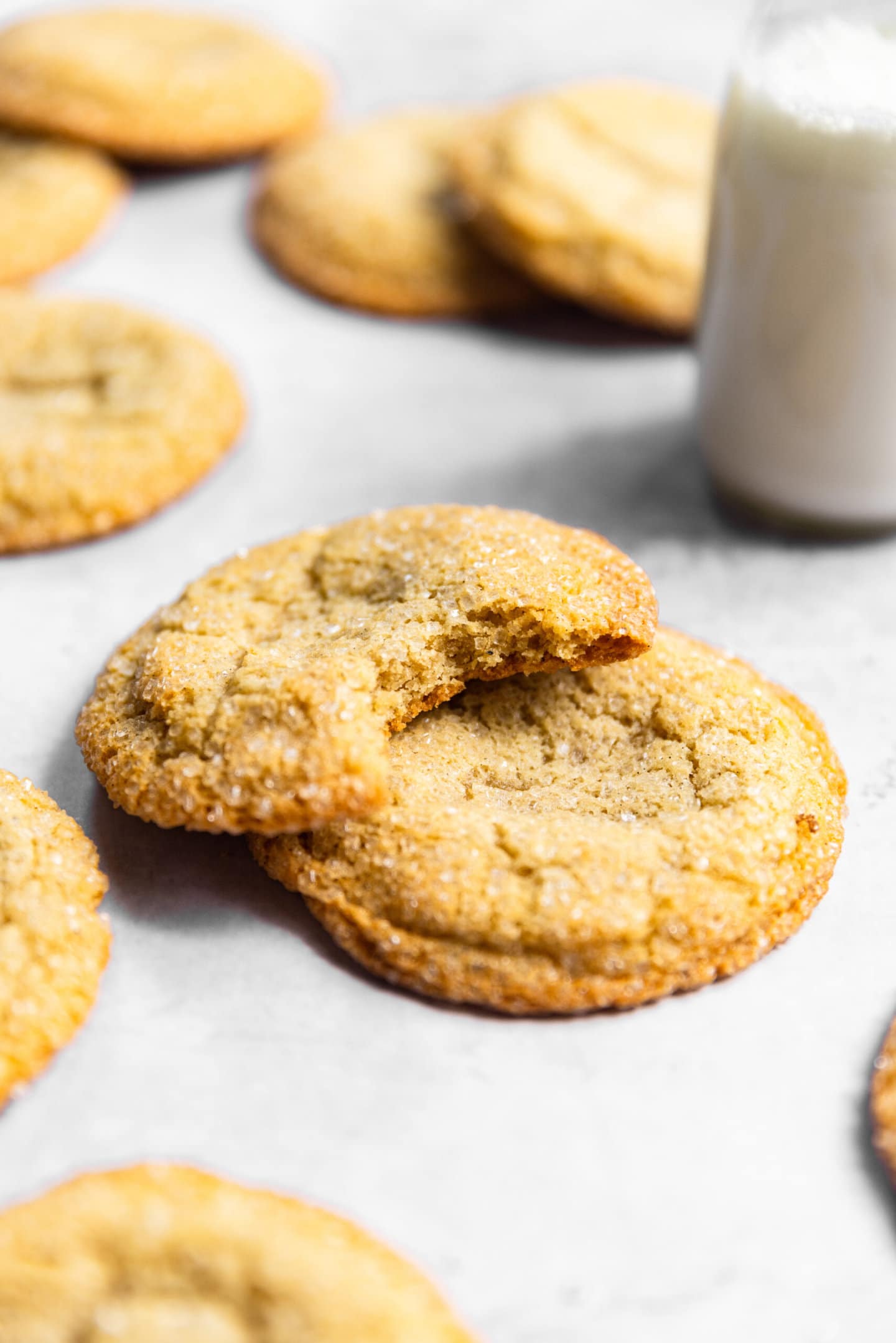 Sugar cookies stacked on top of each other with a bite missing from one next to a glass of milk.