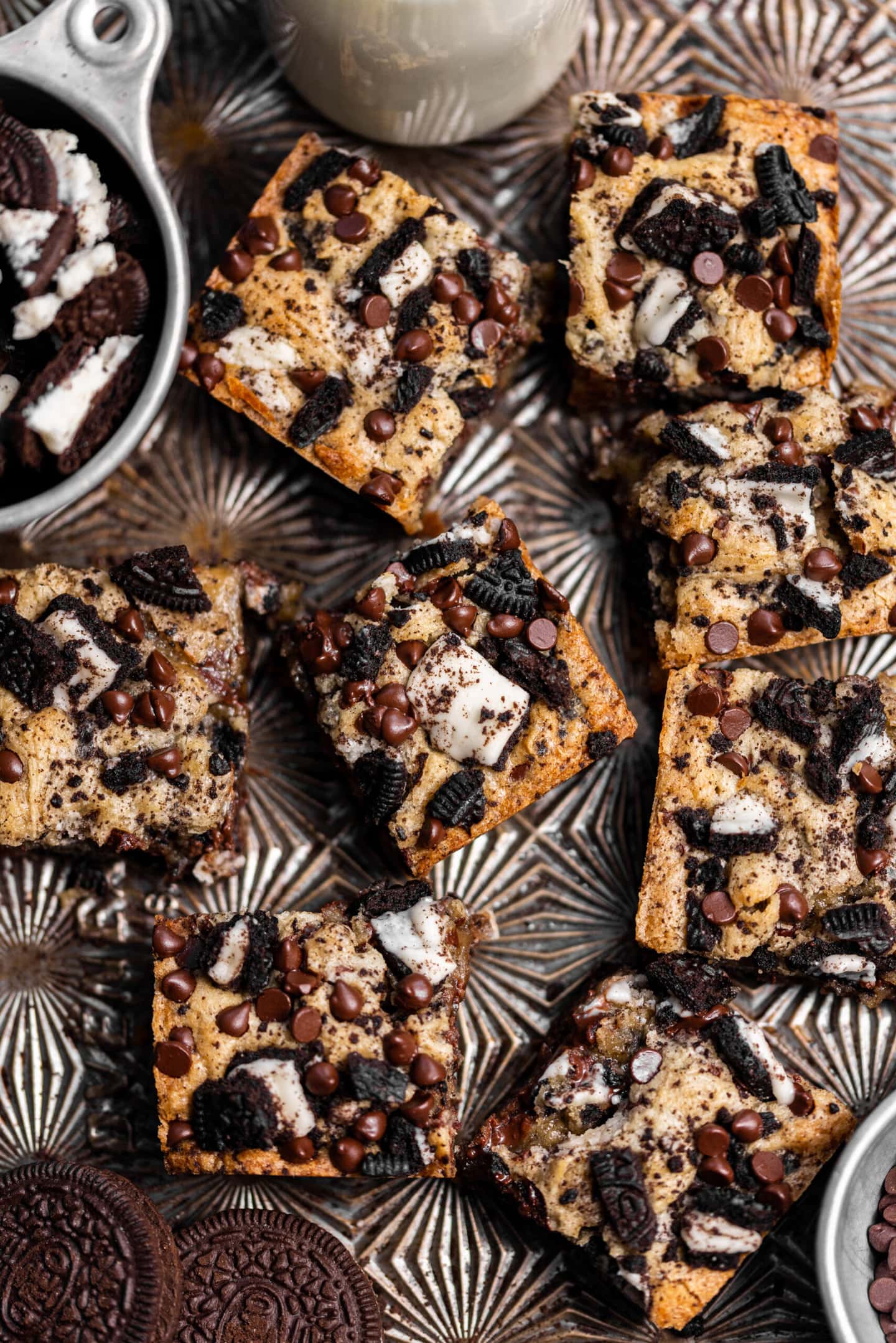 Oreo blondies spread on  a baking sheet next to chopped Oreos and a glass of milk.