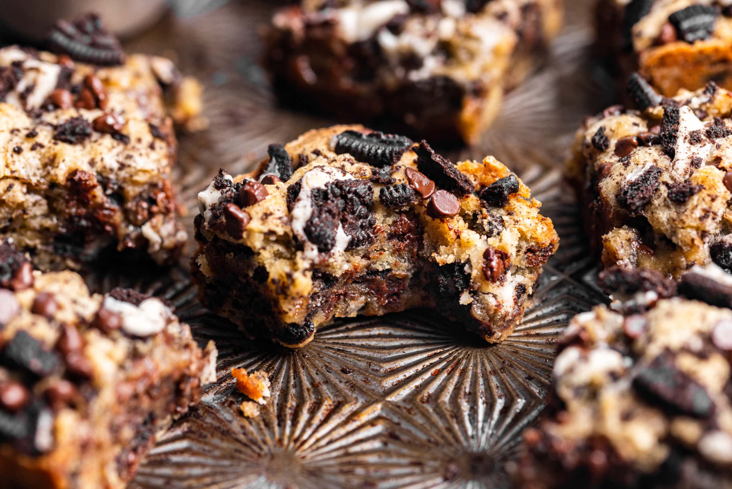 Oreo blondies on a baking sheet with a bite missing from one of them showing gooey texture.