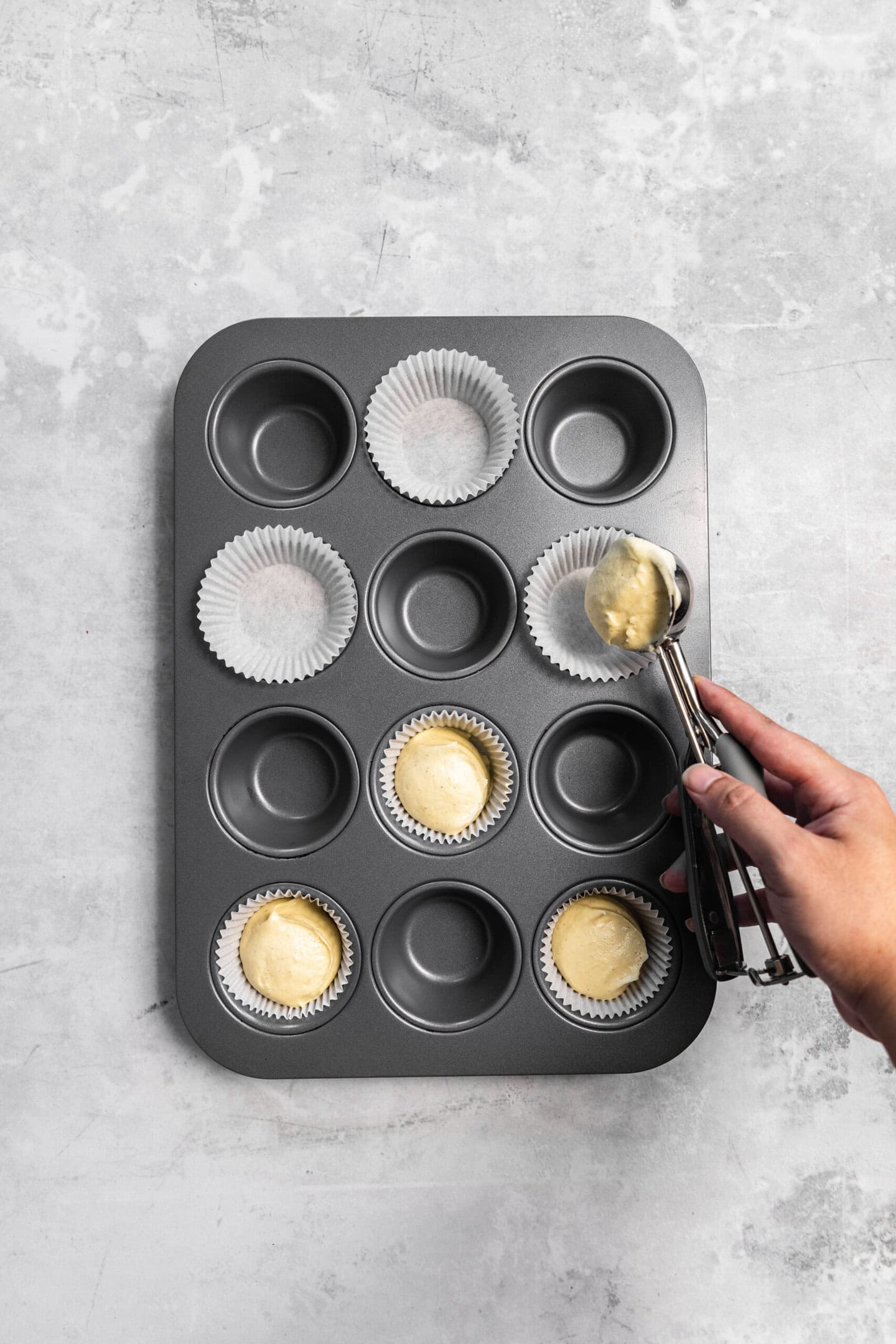 Cupcake batter being scooped into prepared muffin pan.