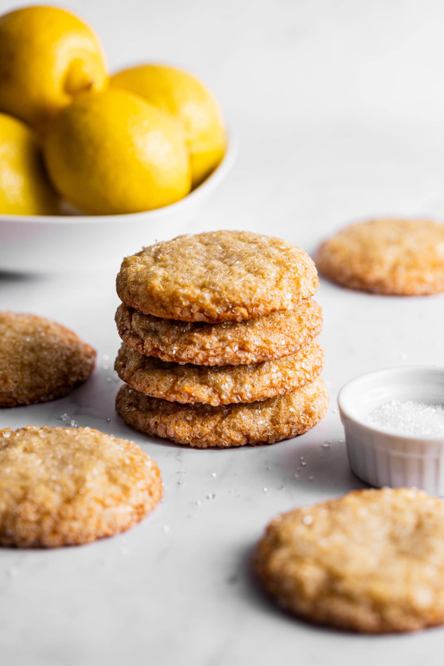 Lemon sugar cookies stacked on top of each other next to a bowl of fresh lemons