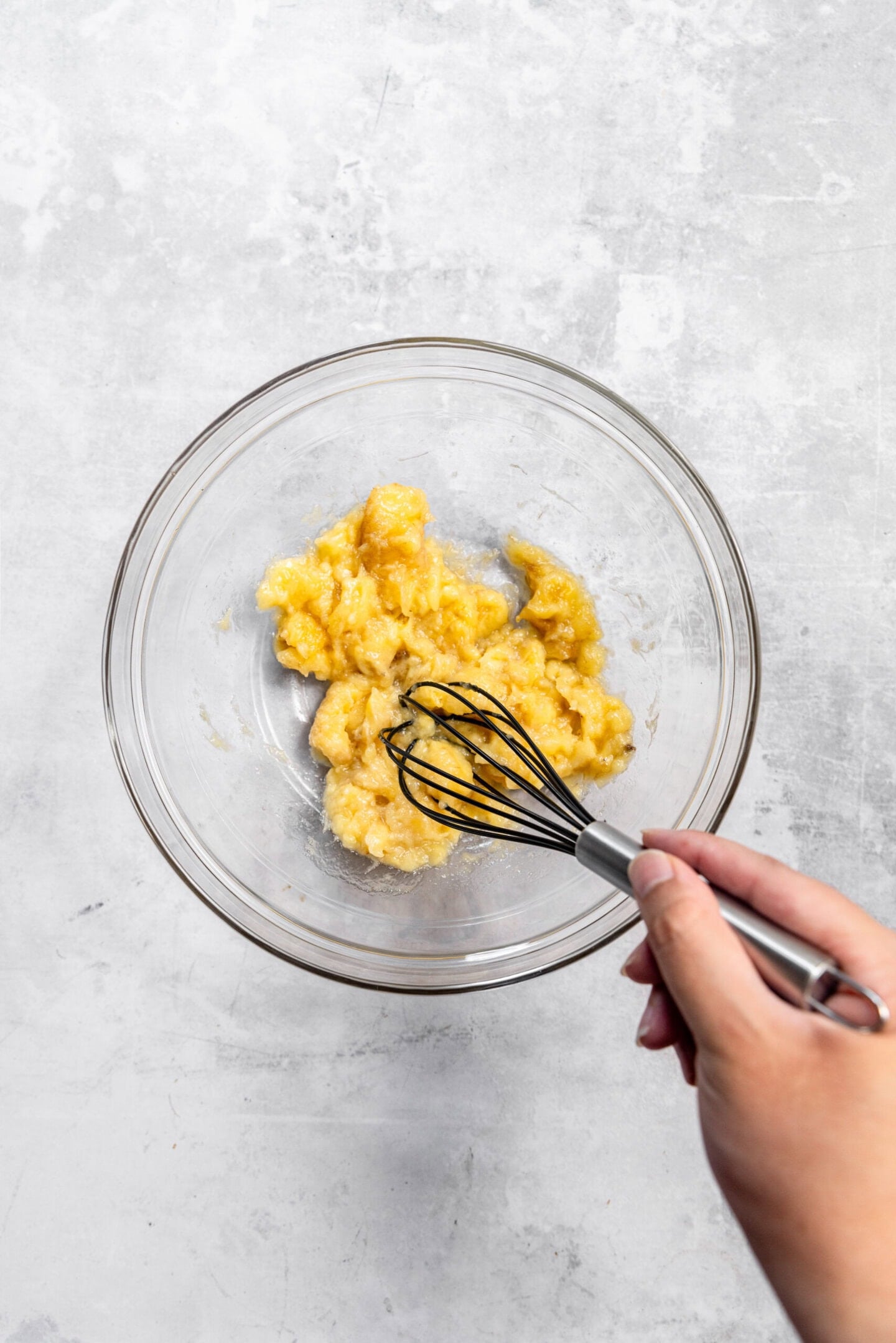 Bananas being mashed by a whisk in a mixing bowl