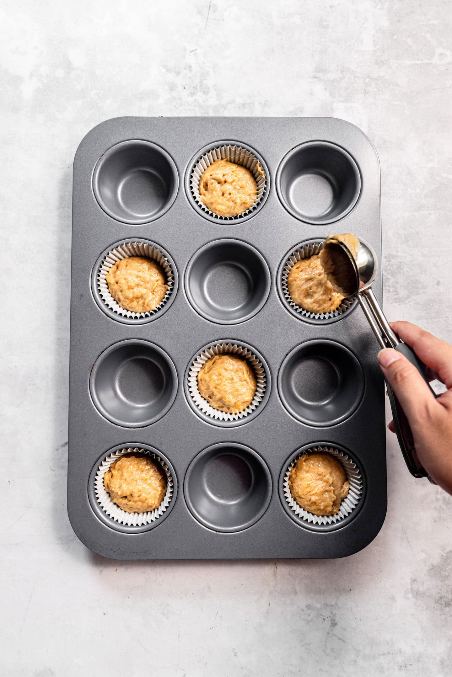 Muffin batter being scooped into a prepared muffin pan
