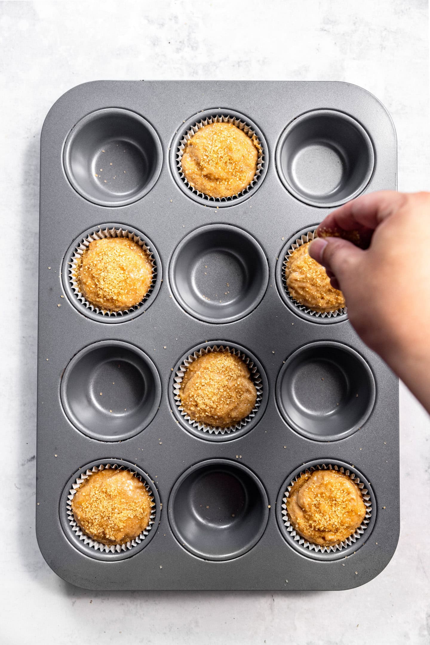 Turbinado sugar being sprinkled on top of muffin batter