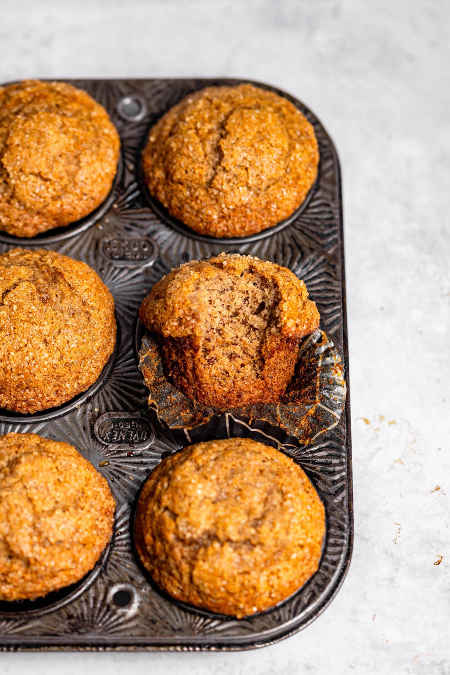 Banana muffins inside a muffin pan with one muffin missing a bite and showing off the interior