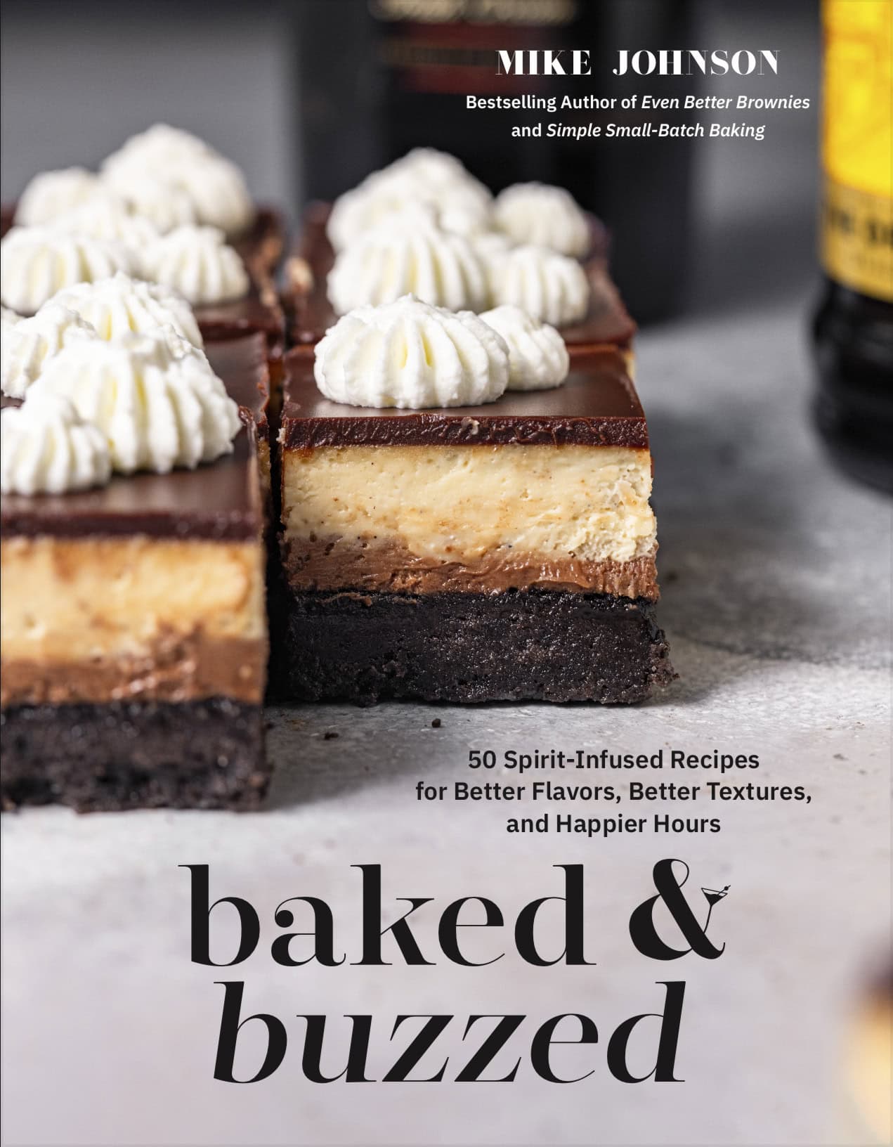 Cookbook cover for Baked & Buzzed, depicting Mudslide Cheesecake Bars with whipped cream piped on top next to bottles of Baileys and Kahlua.