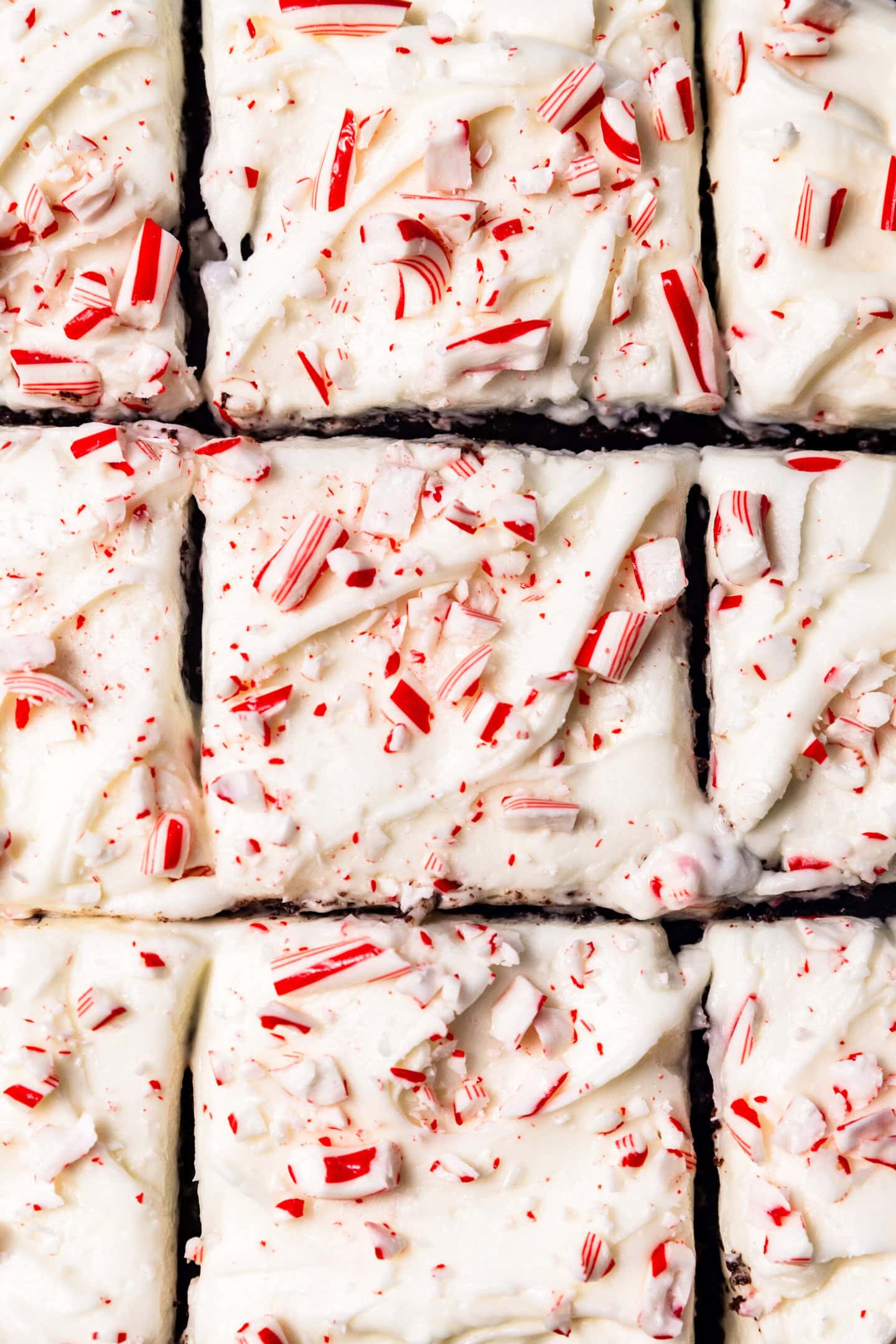 A close up of peppermint cream cheese frosting swirled on top of a chocolate cake with crushed candy canes sprinkled on top.
