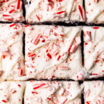 A close up of peppermint cream cheese frosting swirled on top of a chocolate cake with crushed candy canes sprinkled on top.