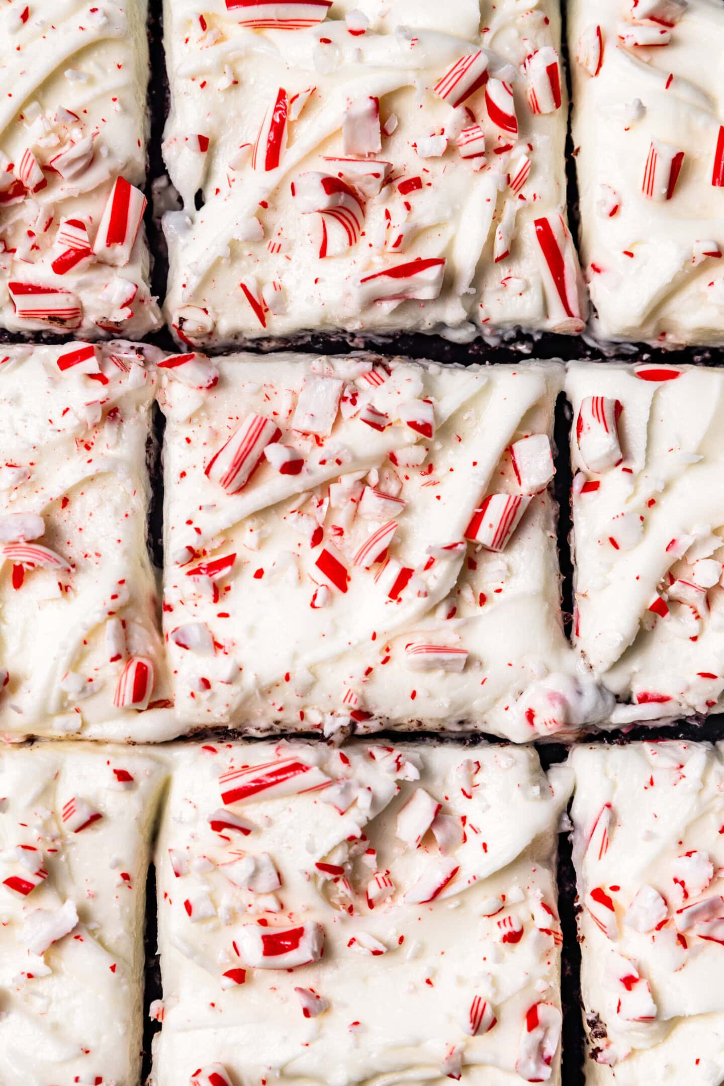 Close up of peppermint cream cheese frosting swirled on top of cake with crushed candy canes sprinkled on top.
