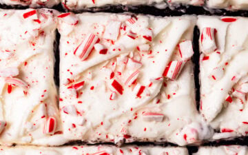 A close up of peppermint cream cheese frosting swirled on top of a chocolate cake with crushed candy canes sprinkled on top.