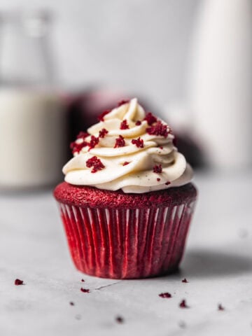 A close up of a single red velvet cupcake topped with a swirl of cream cheese frosting