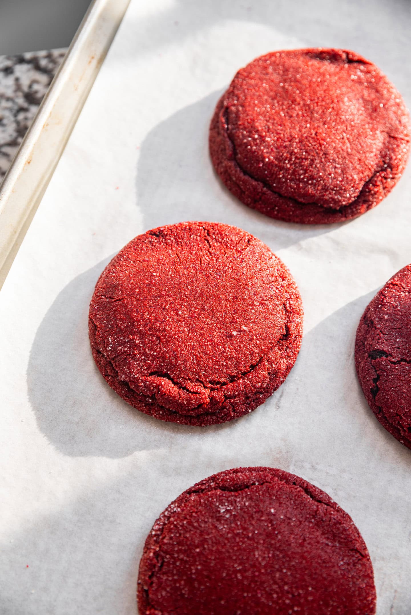 Freshly baked cream cheese stuffed red velvet cookies on a baking tray cooling on a kitchen counter.