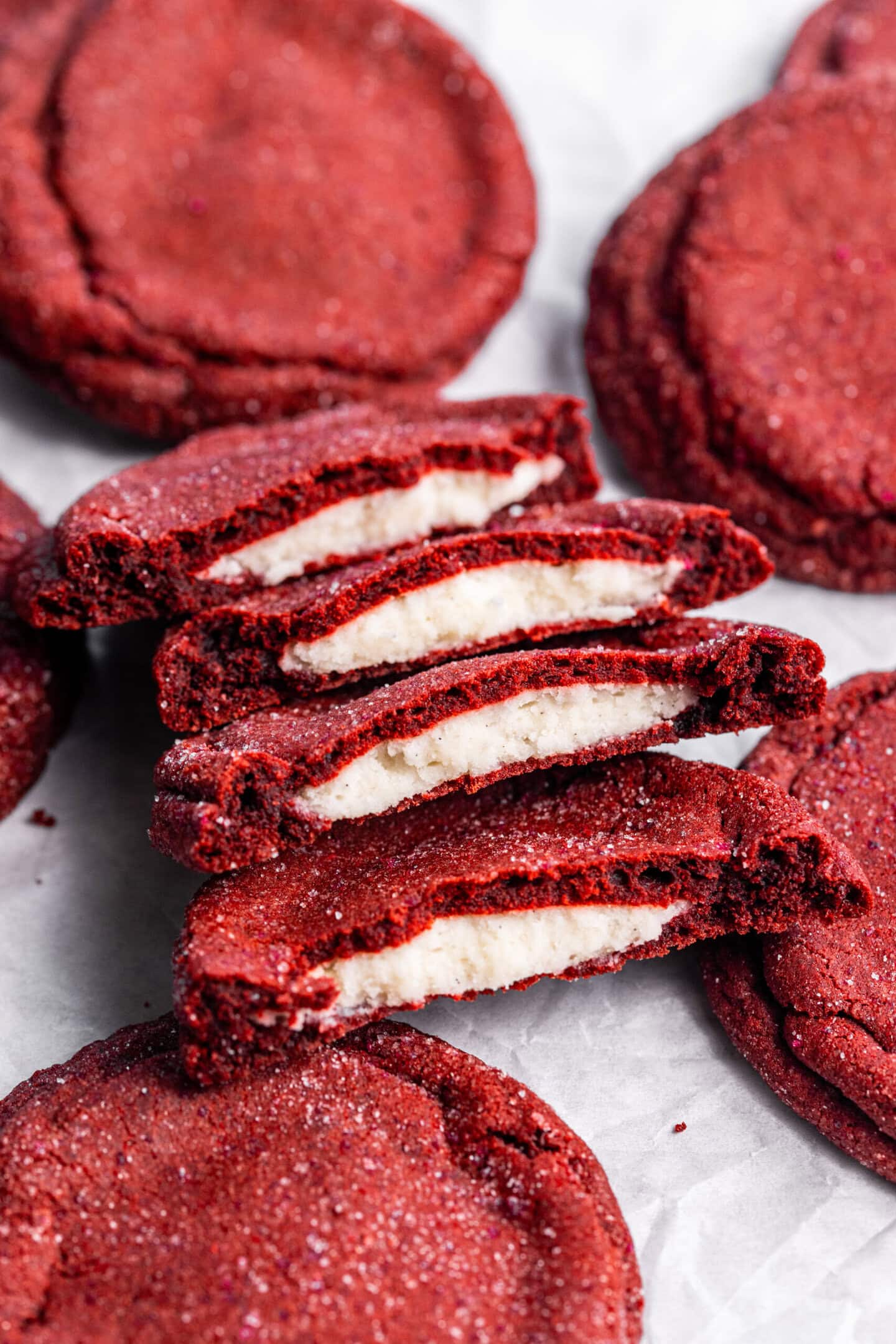 Cream cheese stuffed red velvet cookies on top of parchment paper; some are split in half showing off the cream cheese filling in the center.