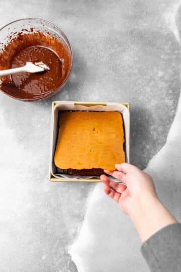 Frozen cookie butter being placed on top of half of the brownie batter.