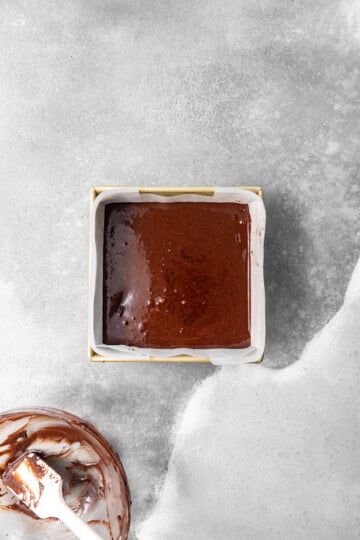 Remaining brownie batter being spread over the frozen cookie butter layer.