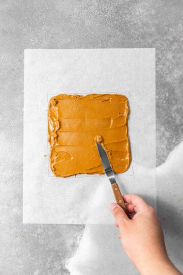 Biscoff being spread into an even square layer on top of parchment paper.