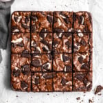 Oreo Brownies on top of parchment paper with pieces of Oreo cookies and a glass of milk and napkin nearby.