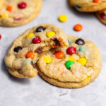 Close up of freshly baked M&M cookies with a bite missing from one showing off soft, chewy interior.