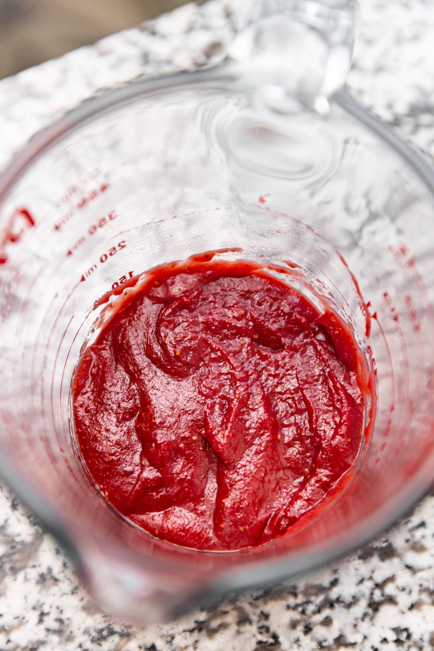 Reduced strawberry paste sitting in a glass measuring cup.
