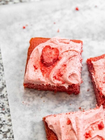 Close up of a slice of strawberry sheet cake with strawberry cream cheese frosting on top and crushed freeze-dried strawberries sprinkled on top.