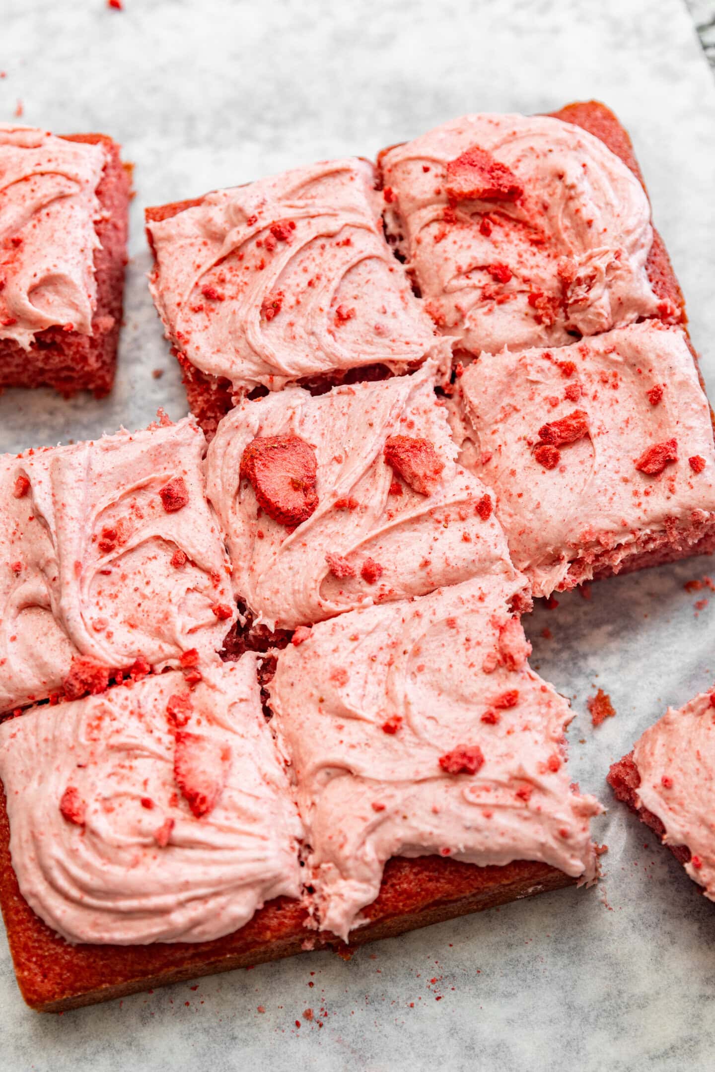 Sliced strawberry snack cake with strawberry cream cheese frosting on top.