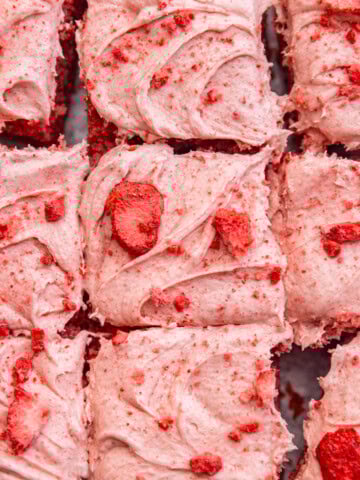 Close up of strawberry cream cheese frosting on top of a cake with chopped freeze dried strawberries sprinkled on top.