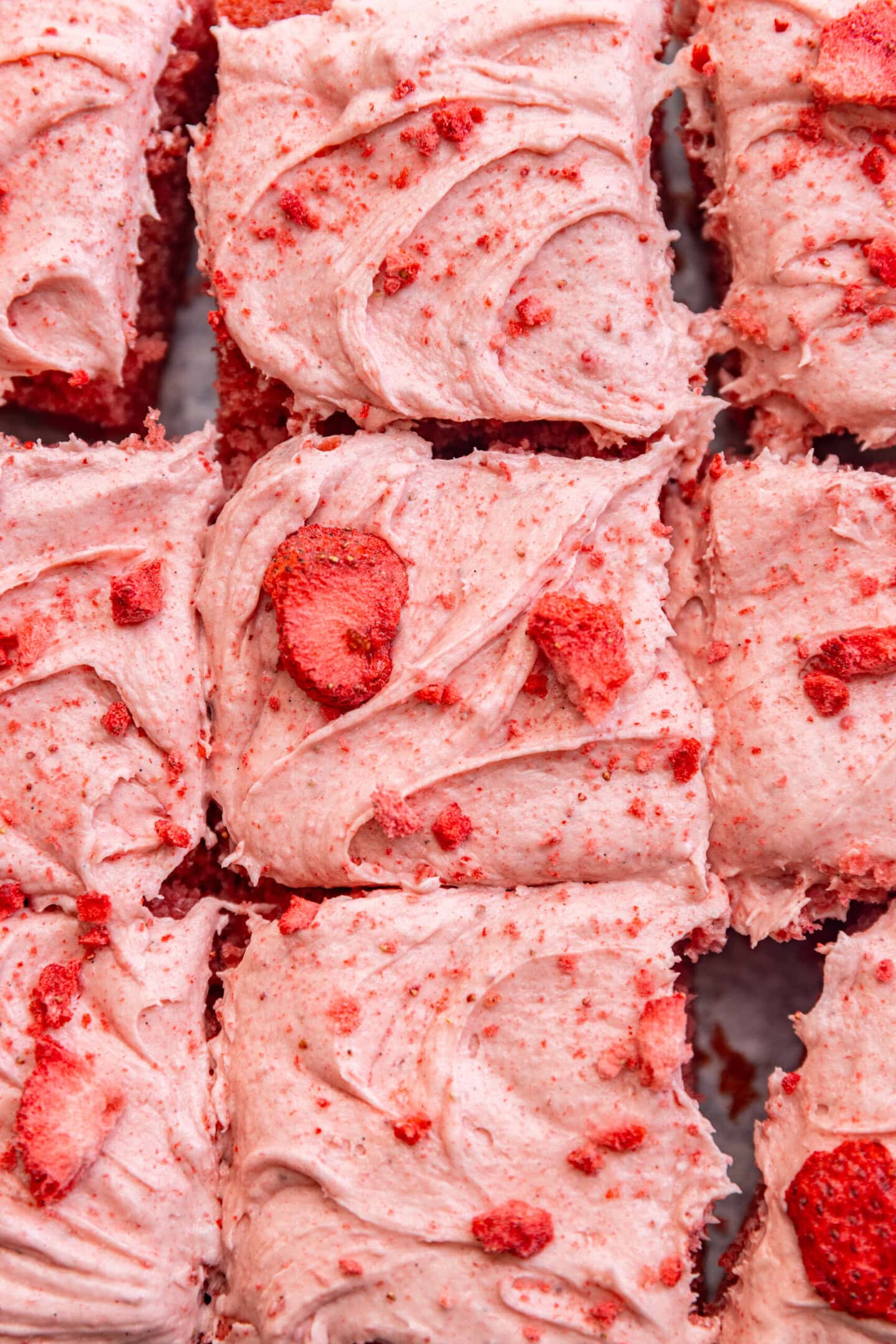 Close up of strawberry cream cheese frosting on top of a cake with chopped freeze dried strawberries sprinkled on top.