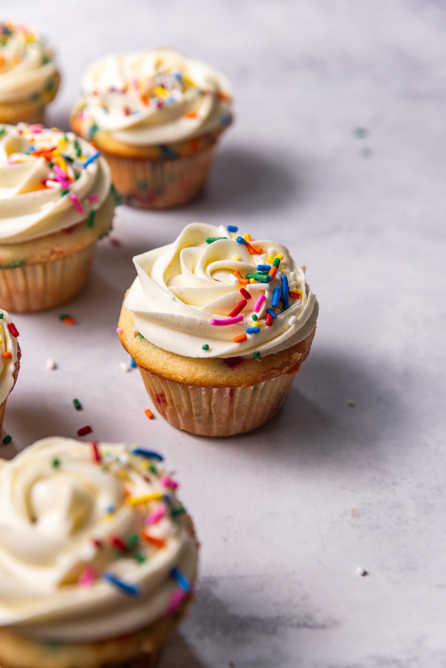 Six Moist Small Batch Funfetti Cupcakes with double vanilla buttercream piped on top and rainbow sprinkles sprinkled on.