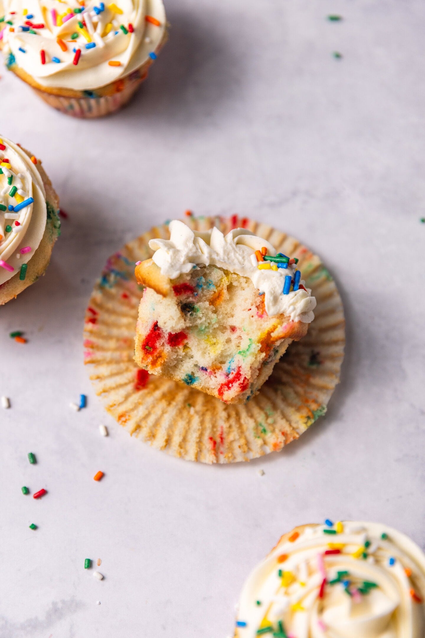 Close up of funfetti cupcake with a bite missing showing off soft and fluffy texture and pops of color from rainbow sprinkles.